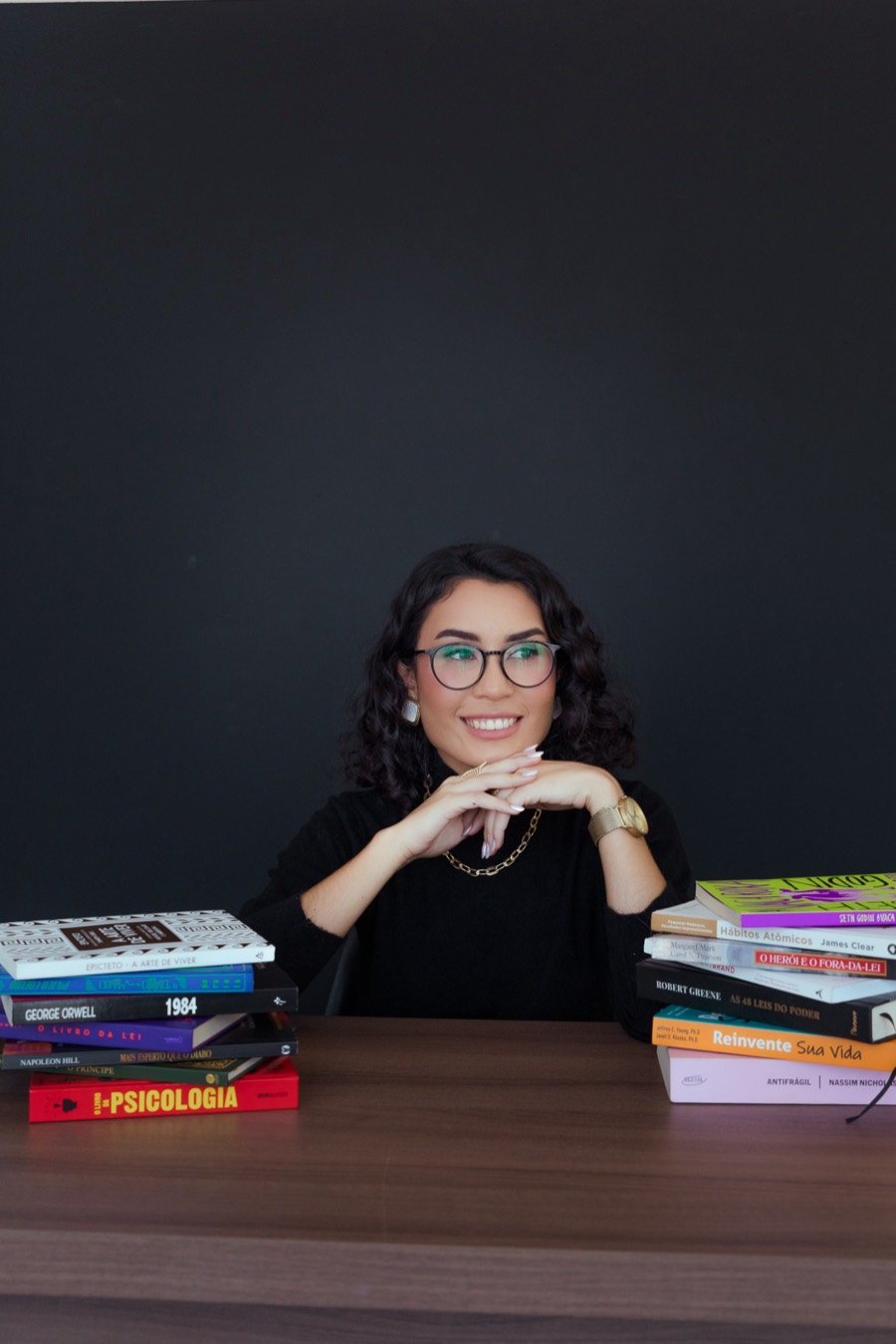 Jullìa Guimarães de óculos, sorrindo entre pilhas de livros